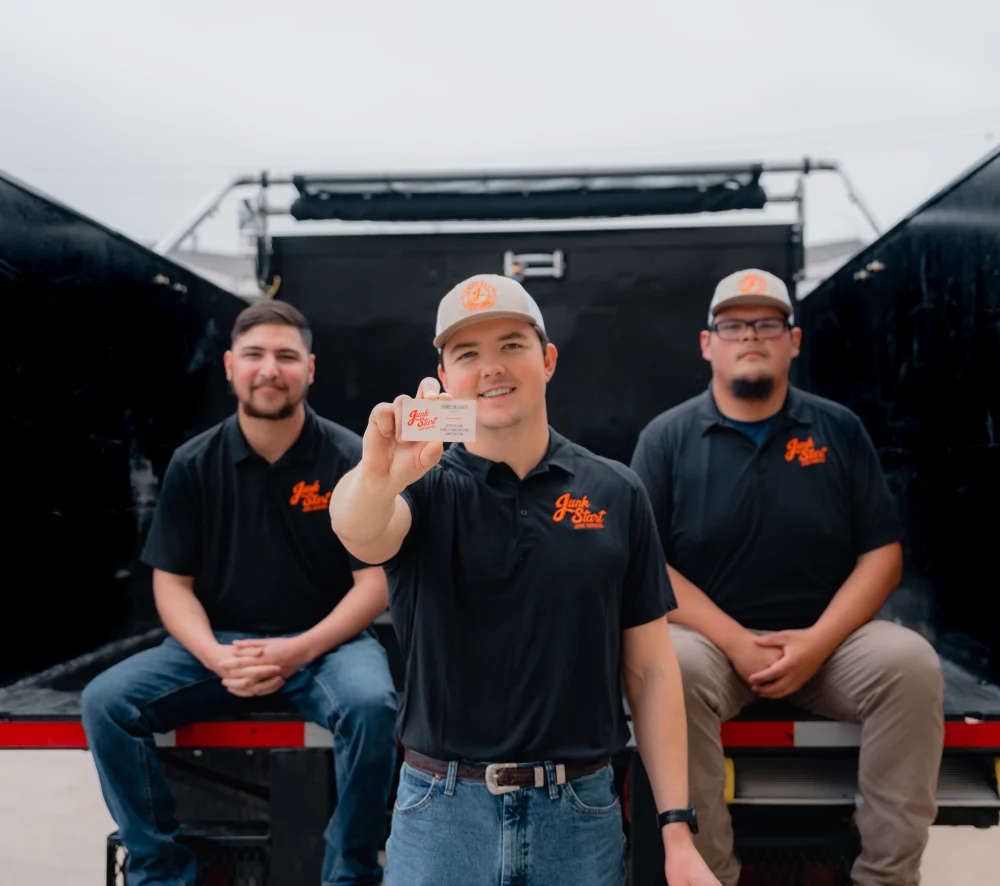 Three Junk Start employees sit on a truck, one holding up a business card. TITLE: