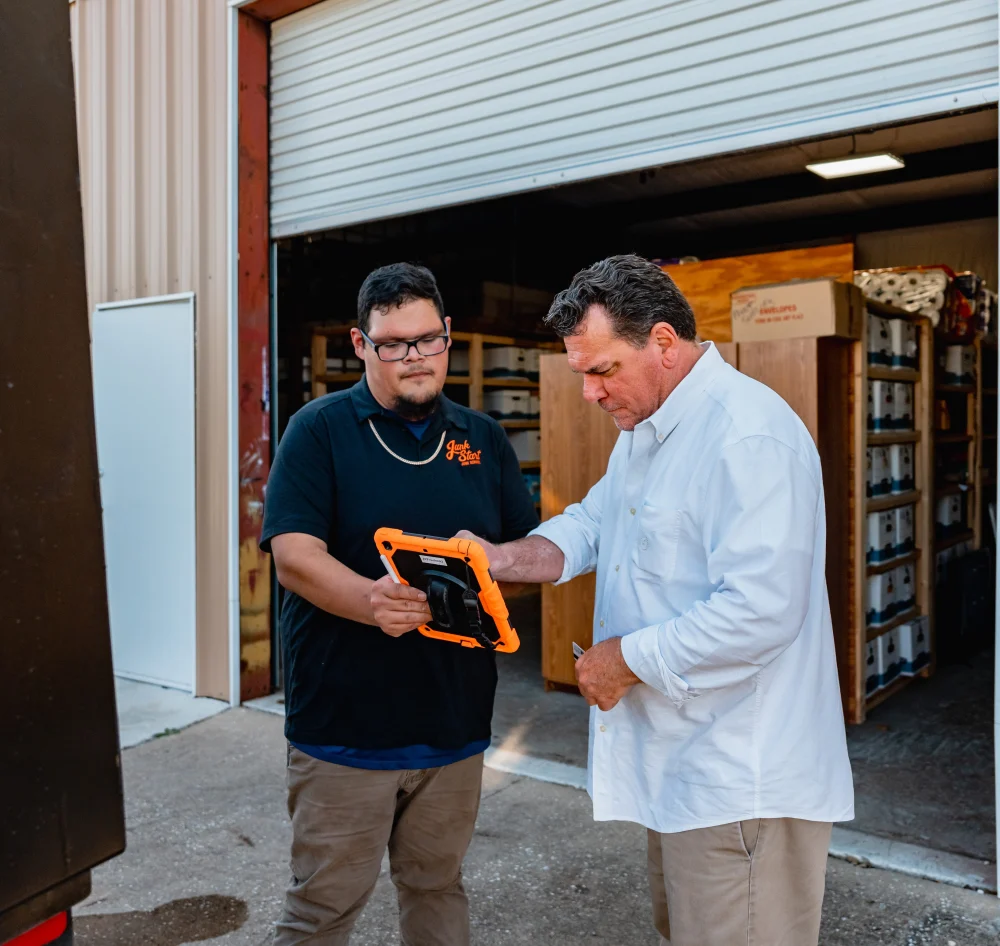 Two men from Junk Start review information on a rugged tablet outside their warehouse.