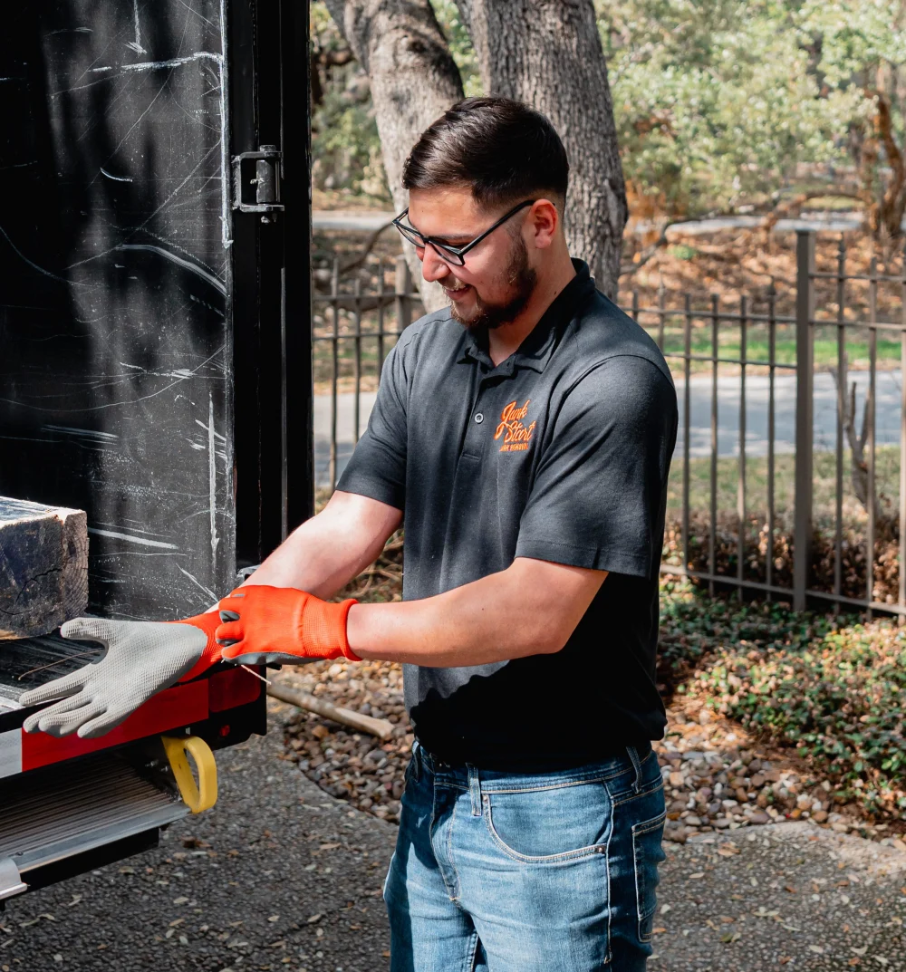 A man in a Junk Start uniform puts on orange work gloves next to a junk removal truck