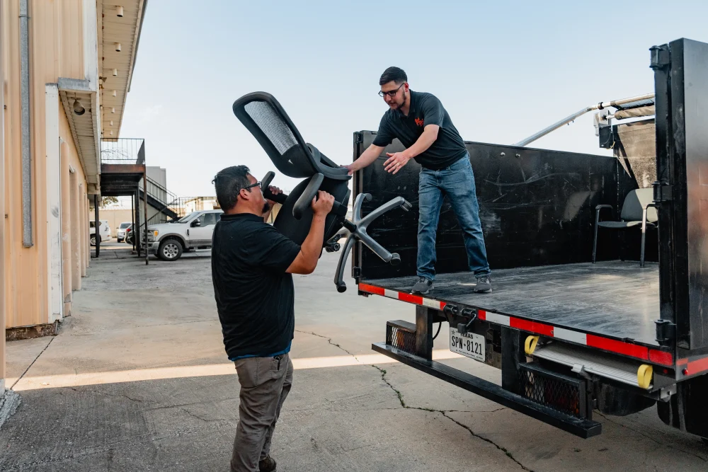 Two men load a black office chair onto the back of a truck. TITLE