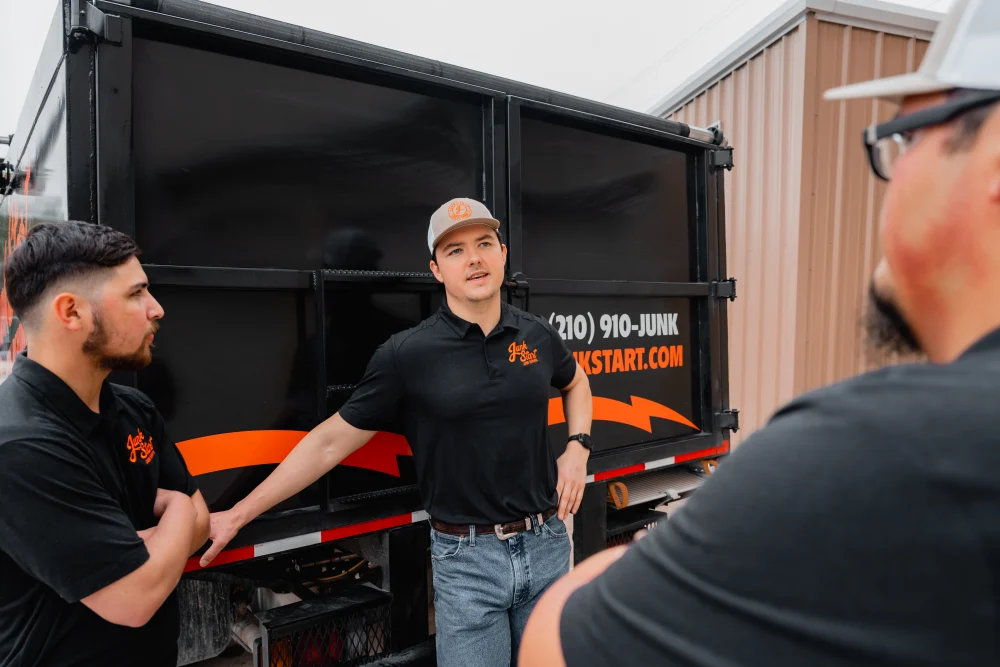 Three Junk Start team members discuss beside their branded black and orange junk removal truck. TITLE