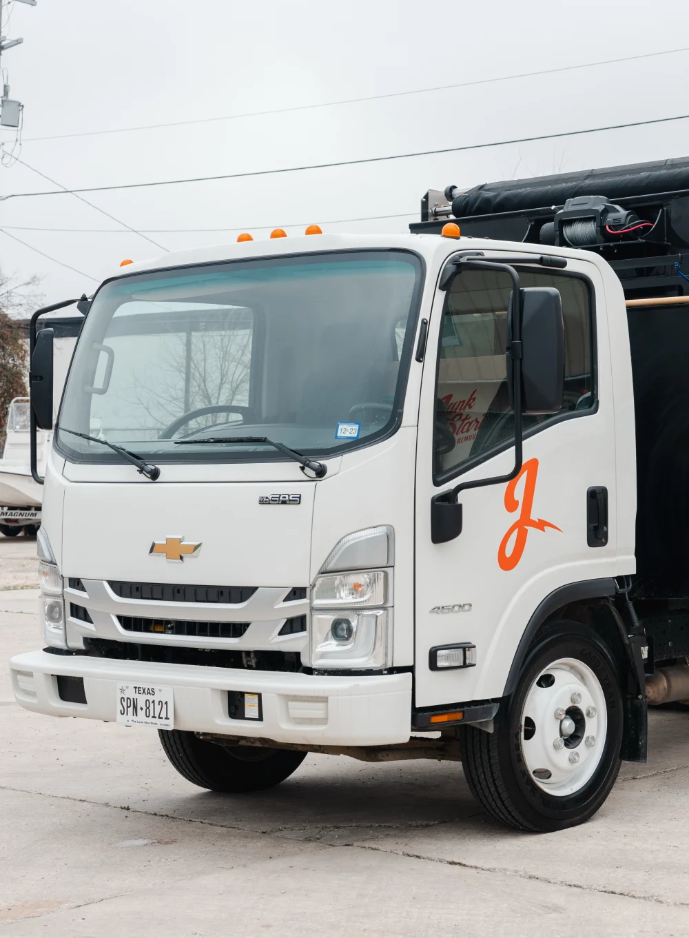 A white Chevrolet commercial truck with an orange "J" logo and black utility body is parked on