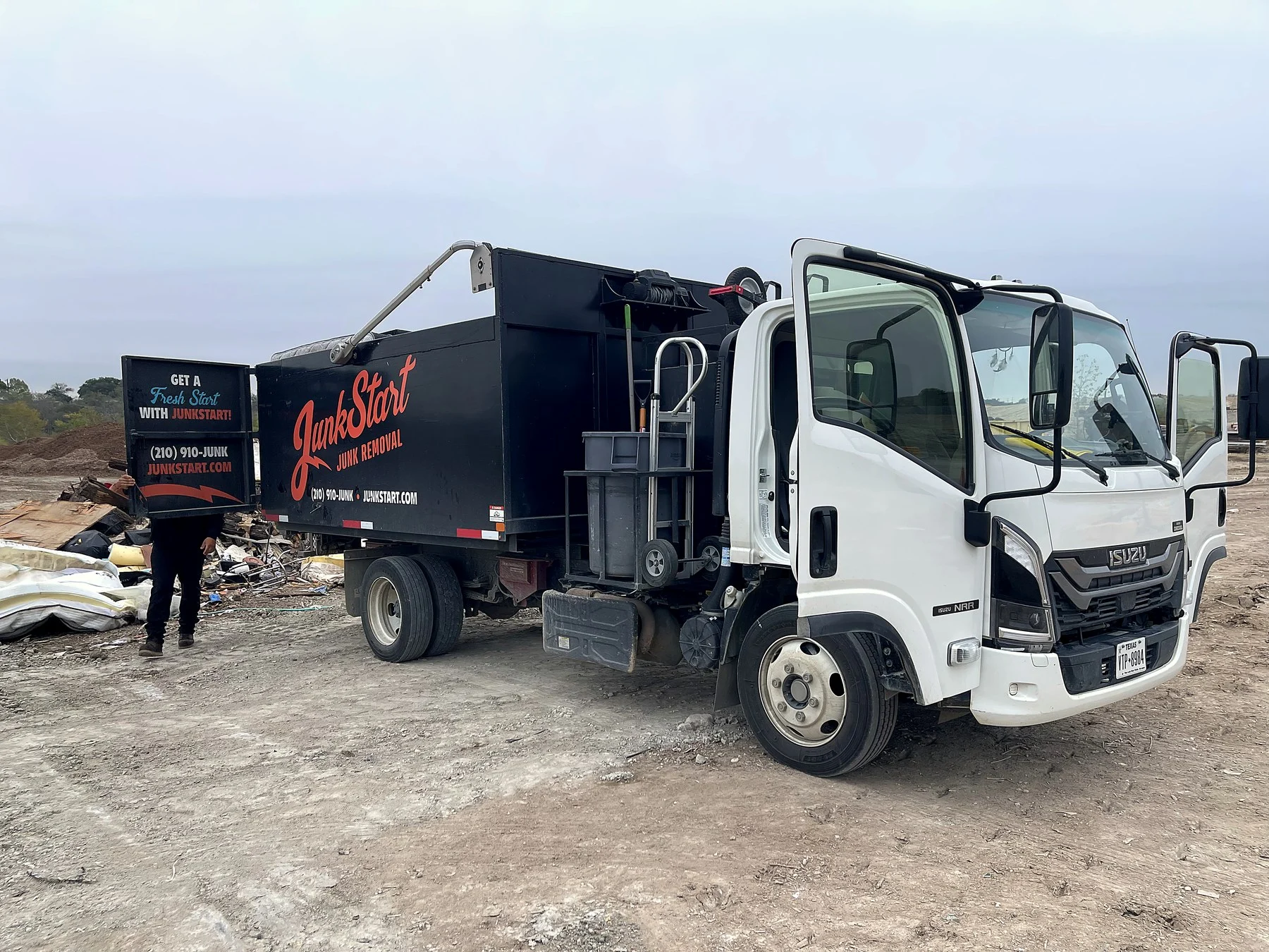 A white Isuzu Junk Start junk removal truck with open doors is parked on a