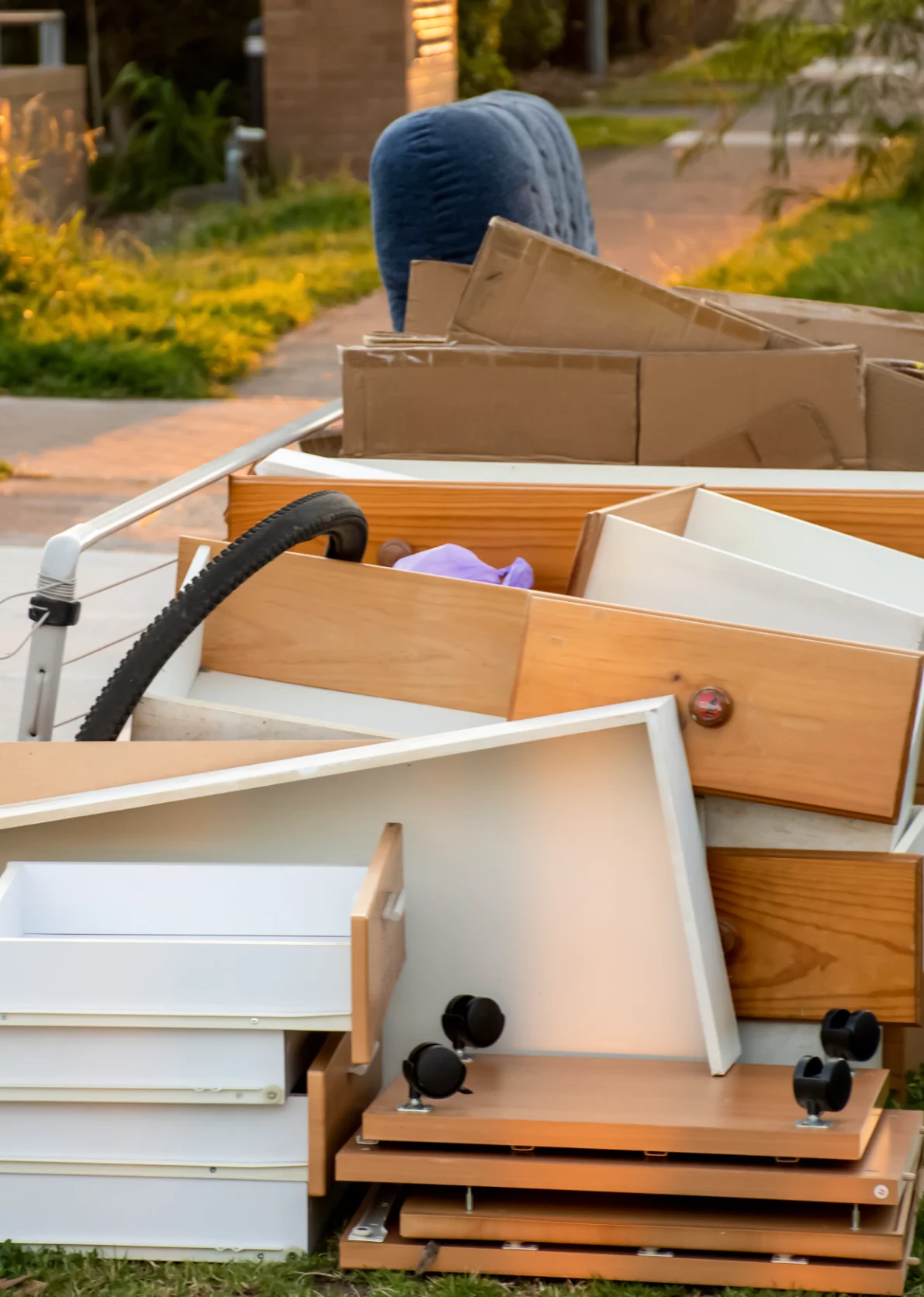 A collection of discarded furniture pieces, cardboard boxes, and household items is piled on a