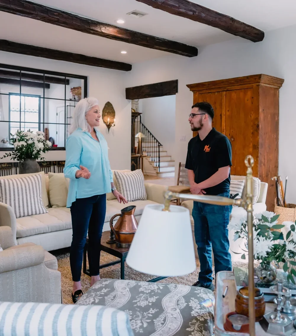 A woman and a service professional converse in a bright, rustic living room with exposed wooden beams