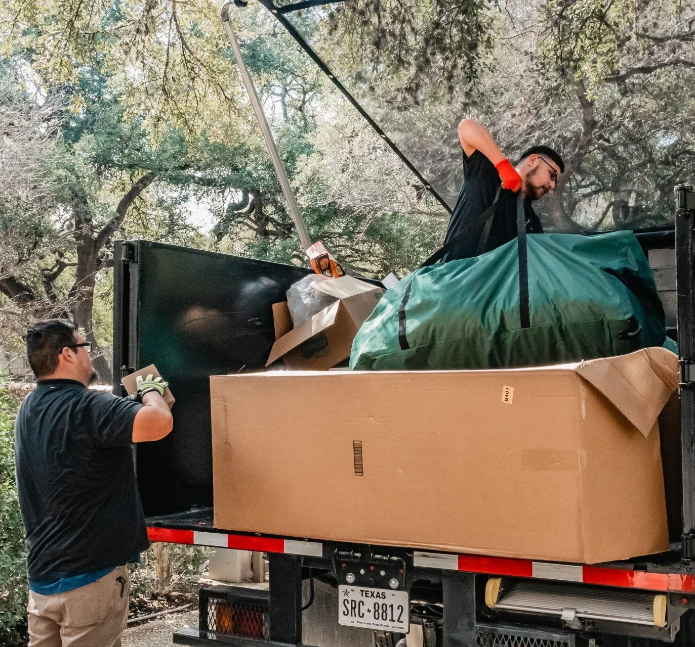 Two movers load a truck with boxes and a large green bag.