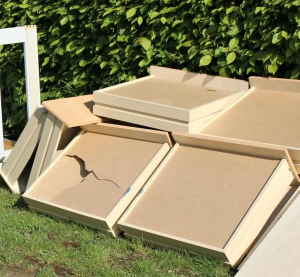 An old armchair, broken cabinet, and wooden drawers are left on a grassy roadside.