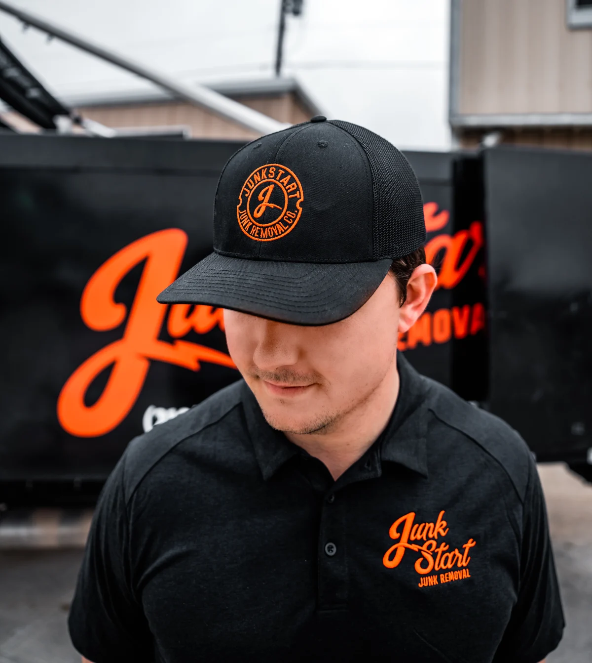 An employee wearing a black Junkstart Junk Removal hat and polo shirt stands in front of