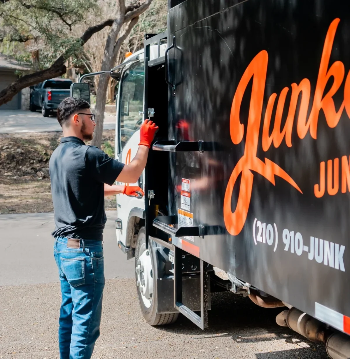 A worker in red gloves stands beside a black Junk Star junk removal truck.