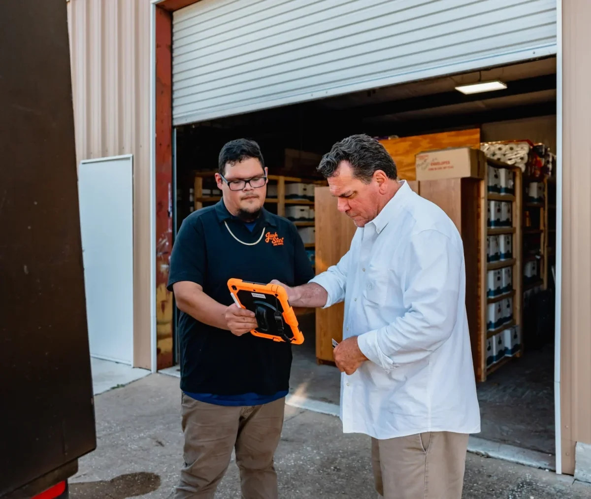 A Junk Start employee shows a client information on a rugged tablet outside a warehouse. TITLE: