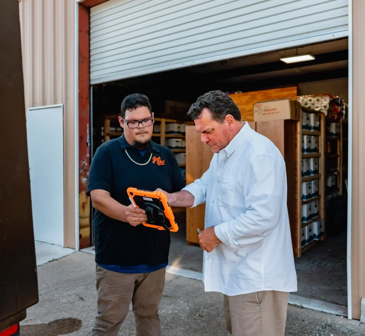 A "Junk Start" employee shows a client information on a rugged tablet outside a warehouse.