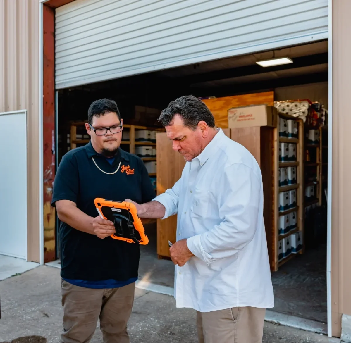 A Junk Start employee shows a client details on a rugged tablet outside a commercial storage facility.