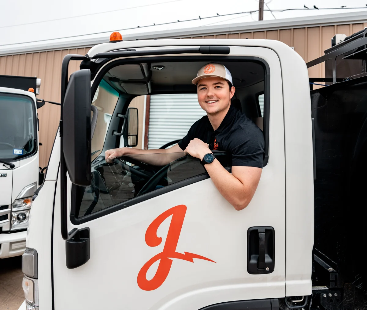 A smiling young man in a cap and polo shirt sits in a white service truck