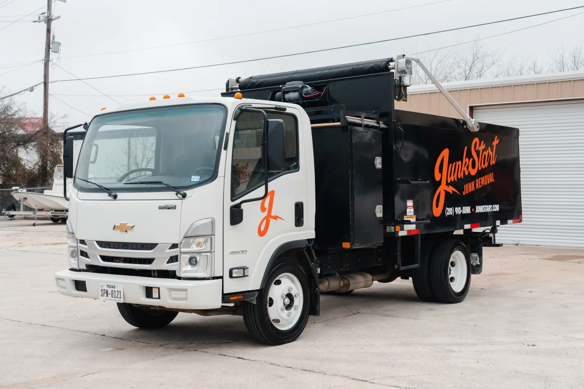 A white Chevrolet JunkStart junk removal truck with orange branding is parked on a concrete lot.
