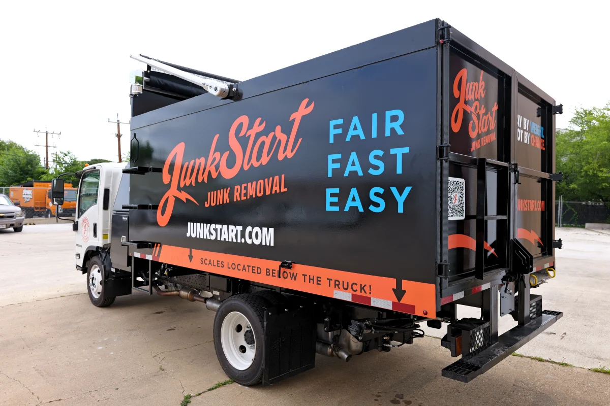 A black JunkStart junk removal truck with orange and blue branding is parked on concrete.