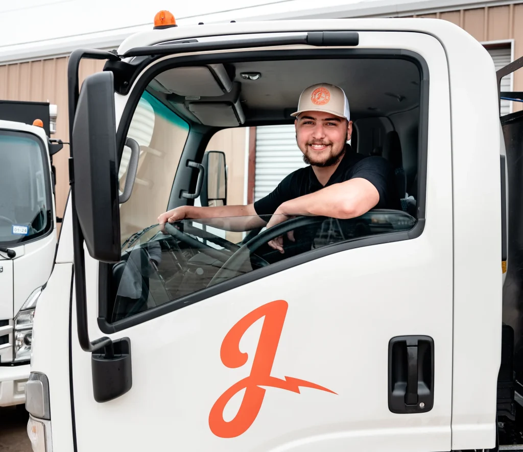 Smiling man in a baseball cap sits in the driver's seat of a white truck with an