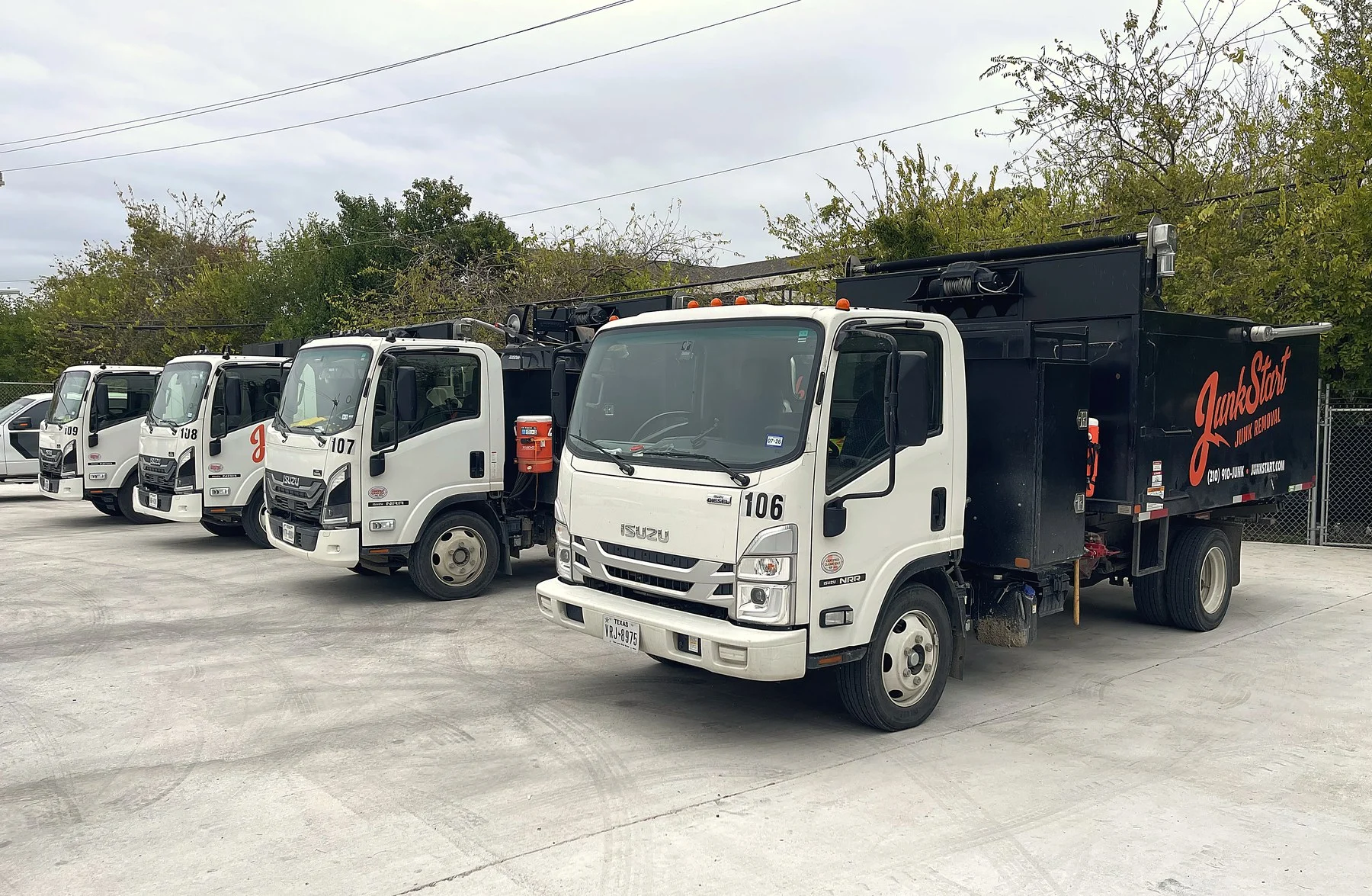 Several white Isuzu JunkStart junk removal trucks with black beds are parked in a lot.