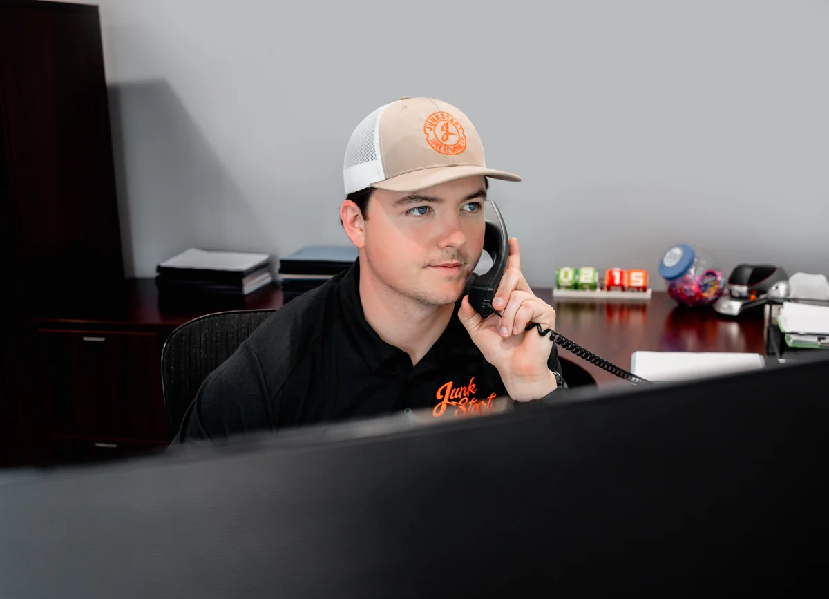 A Junkstart employee wearing a branded hat and shirt speaks on a landline phone at his office