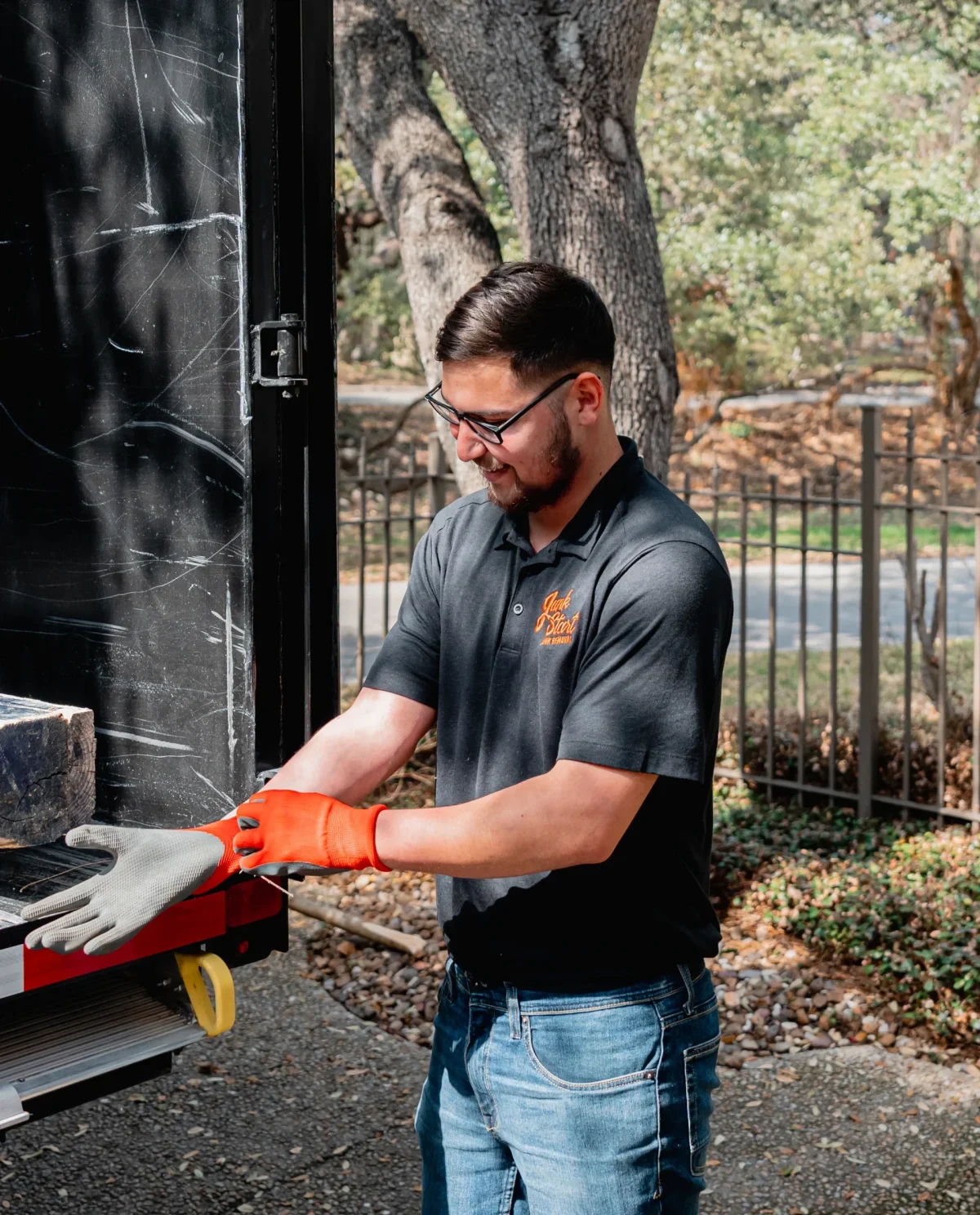 A man in a Junk Start shirt puts on orange work gloves by a truck.