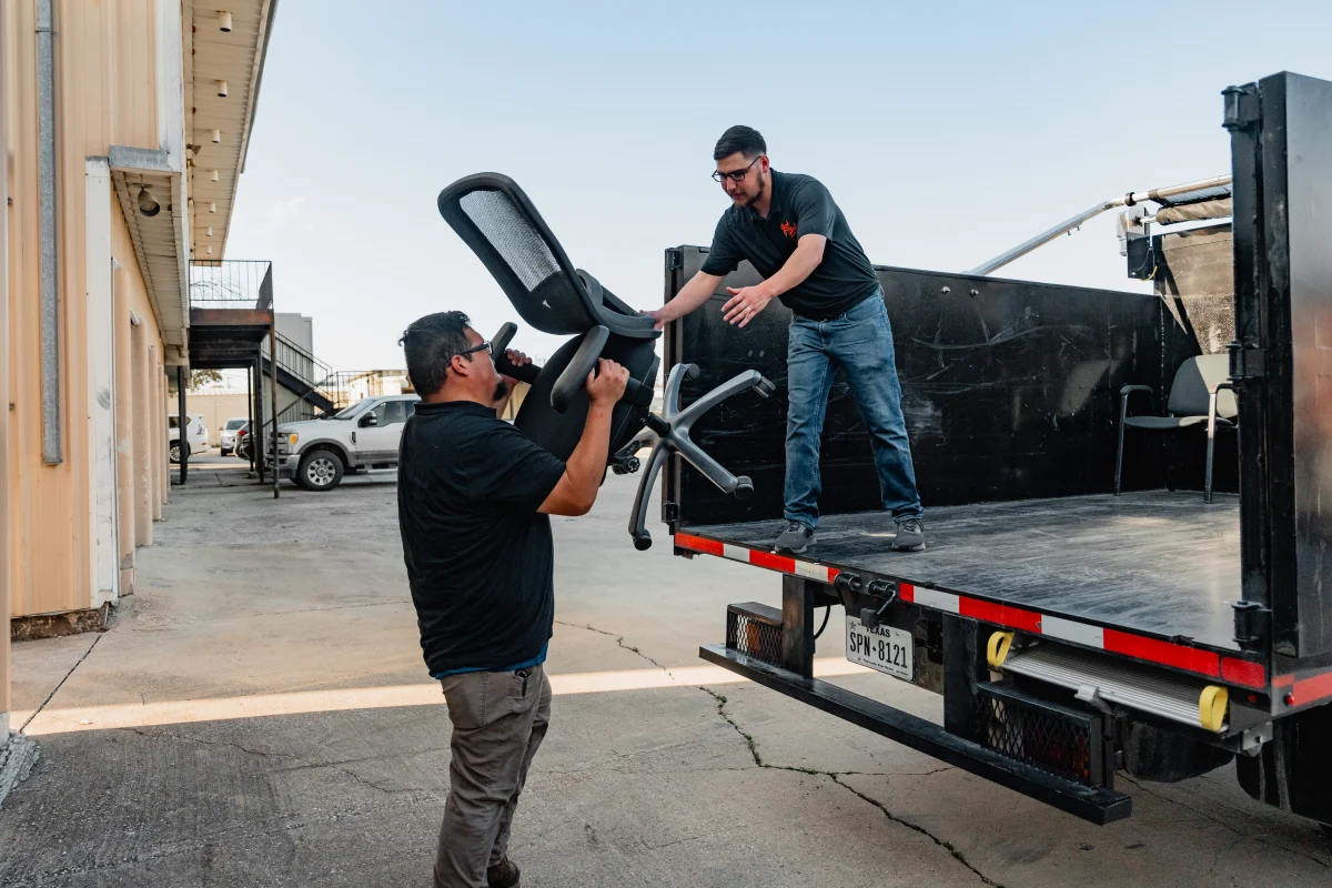 Two men are loading a black office chair into the back of a black truck. TITLE: