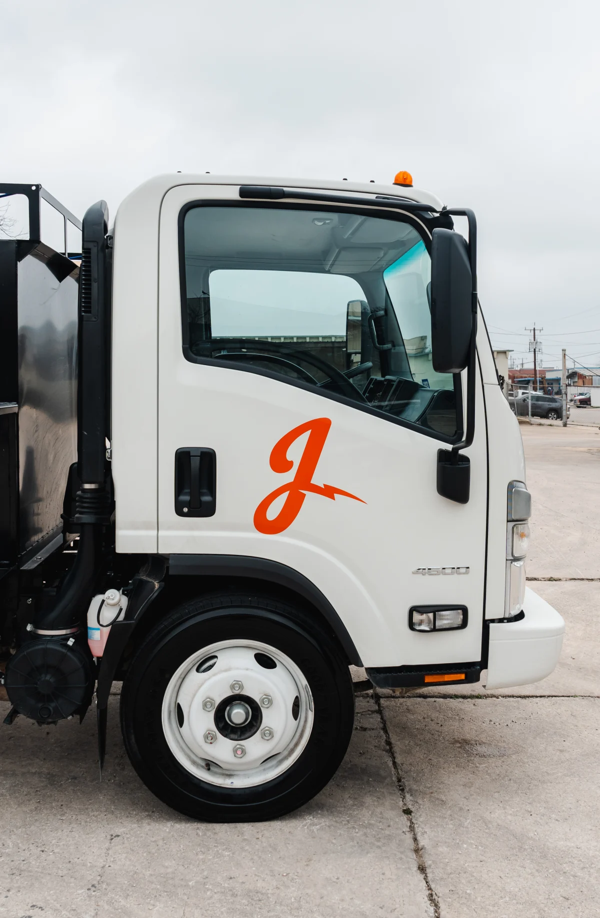 A white utility truck with an orange "J" logo and amber warning light is parked on